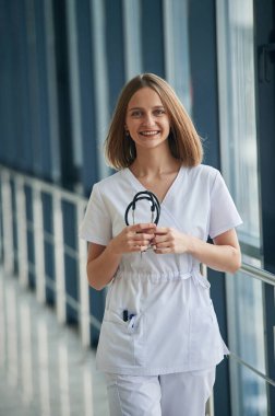 Profesyonel steteskop ellerinde. Beyaz önlüklü kadın doktor koridorda..