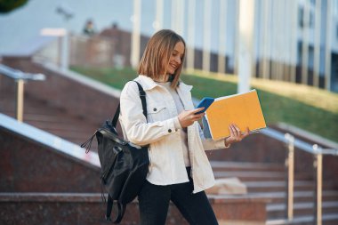 Akıllı telefon elindeydi. Gündelik giysiler içinde genç bir kız öğrenci dışarıda..