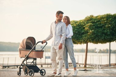 Arkadaki küçük yeşil ağaçlar. Bebek arabalı genç bir çift birlikte yürüyor.. 