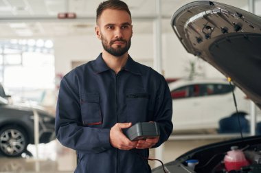 Elektriği ölçmek için bir aletle. Araba tamircisi otomobille garajda..