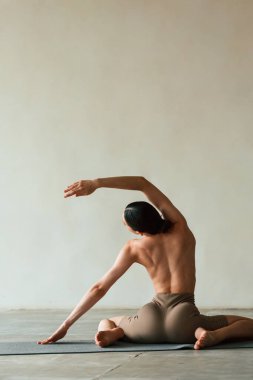 Esnek vücut, oturma, dikiz. Zayıf vücutlu genç bir kadın stüdyoda spor kıyafetleri giyiyor..