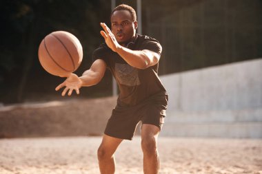 Fotoğraf hareket halinde. Genç siyah adam basketbol topuyla dışarıda..