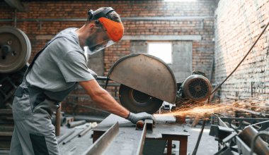 Metali kesmek için elektrikli testere kullanmak. Gri üniformalı genç fabrika işçisi.