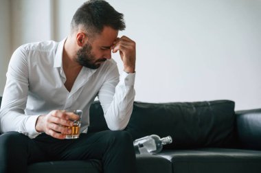 Kanepede oturuyor. Alkolik genç adam içeride..