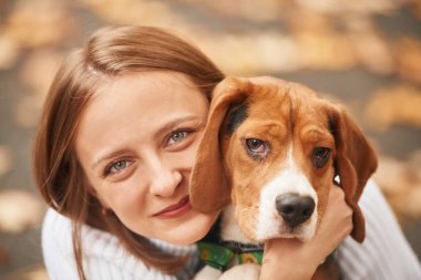 Oturmak, hayvanı tutmak ve kameraya bakmak. Genç kadın köpeğiyle birlikte parkta..