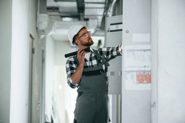 Yan görüş, el feneri kullanmak, elektrik kutusunu kontrol etmek. Üniformalı tamirci tamamlanmamış binada..