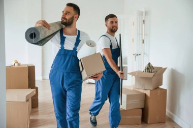 Mat ve resim ellerinde. Bir odada hareket eden iki servis çalışanı.