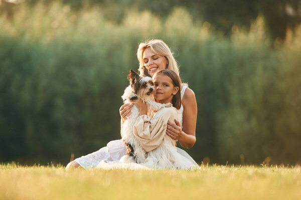 With cute dog. Mother with her daughter are on the field outdoors.