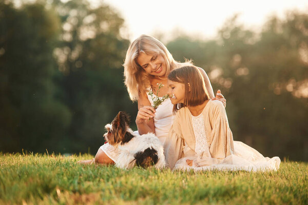 Positive emotions, on the green grass. Mother with her daughter and cute dog are on the field outdoors.