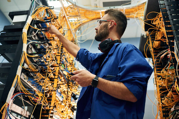 Стабильность сигнала измеряется устройством. Молодой человек работает с интернет-оборудованием и проводами в серверной.