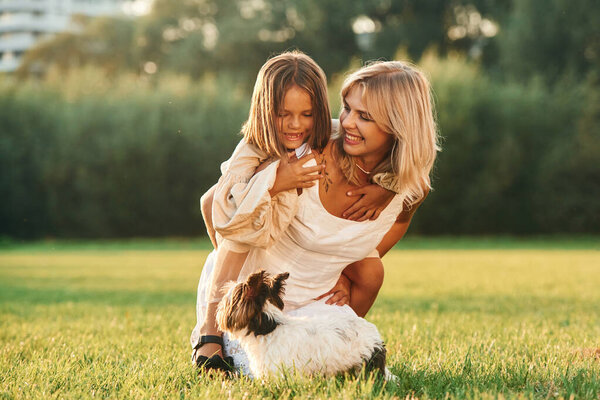Conception of love and care. Mother with her daughter and cute dog are on the field outdoors.