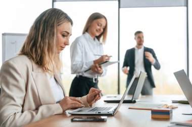 Masadaki dizüstü bilgisayarı kullanarak. Bir grup ofis çalışanı içeride birlikte..