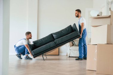 Ağır kanepe tutuyordu. Bir odada hareket eden iki servis çalışanı.