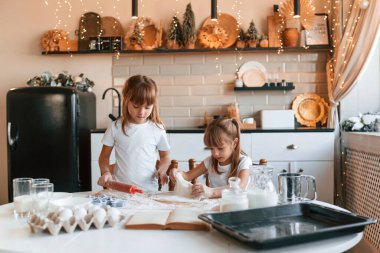 Hamurla çalışmak. İki küçük kız mutfakta çelenklerle yemek hazırlıyor..