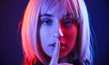 Sessiz olmanın işareti, parmak dudaklardadır. Beyaz saçlı kadın stüdyoda neon renkli..