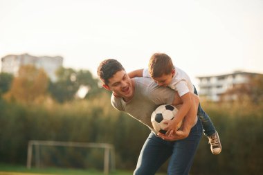 Profesyonel futbol topunu tutuyor. Baba ve küçük oğlu dışarıda oynuyor ve eğleniyorlar..