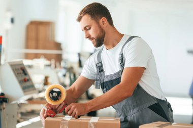 Gri üniformalı. Yakışıklı adam ekolojik kutular üreten fabrikada çalışıyor..