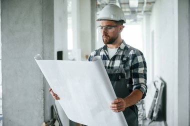 Kağıt üzerinde el ele tutuşarak proje yapın. Bitmemiş odada üniformalı inşaat işçisi..