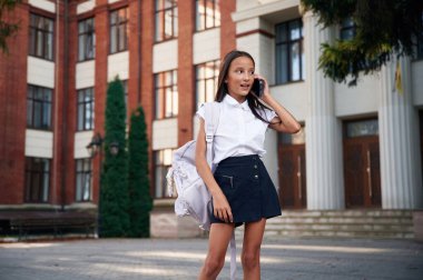 Telefon ellerinde. Okul üniformalı kız binanın yanında..