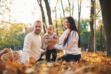 İki ebeveyn, sonbahar parkında küçük tatlı bir çocukla oturuyorlar. Düşen yapraklar ve tereyağı ezmesi üzerinde..