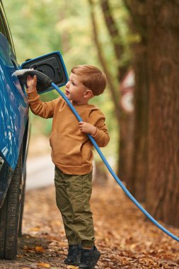 Yoldayım. Şirin genç çocuk mavi elektrikli arabayı dışarıda şarj ediyor..