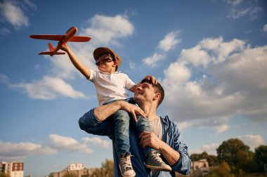 Oyuncak uçakla oynamak, omuzlarda oturmak. Baba ve küçük oğlu dışarıda eğleniyorlar..