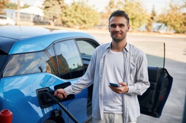 Ön manzara. Şarj istasyonunda mavi elektrikli arabası olan adam..