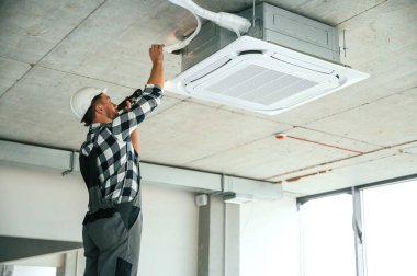 Havalandırma sistemi tamir ediliyor. Üniformalı tamirci tamamlanmamış binada..