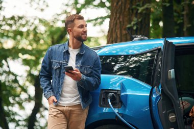 Yakışıklı adam dışarıda elektrikli arabasının şarj olmasını bekliyor..