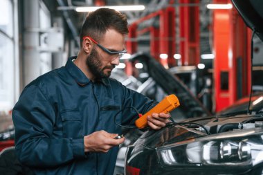 Cihaz kullanarak elektronik aletleri kontrol ediyorum. Araba tamircisi otomobille garajda..