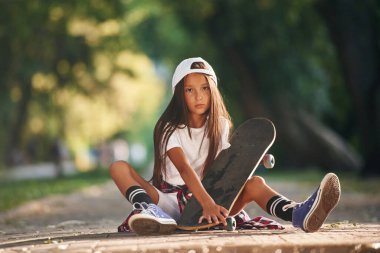 Ön manzara, yerde oturuyor. Dışarıda kaykaylı mutlu küçük kız.