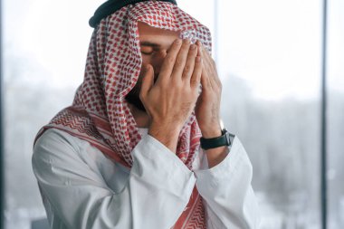 Elleri yüze yakın dua ediyor. Ofisinde geleneksel kıyafetleriyle başarılı bir Müslüman işadamı..