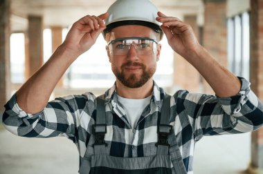 Kasketli bir portre. Bitmemiş odada üniformalı inşaat işçisi..