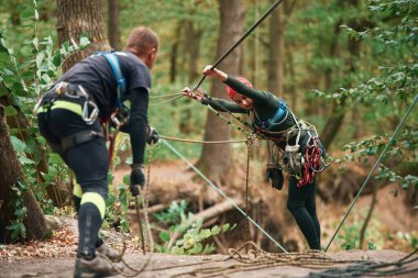 İpleri hazırlıyorum. Erkek ve kadın ormanda güvenlik malzemesi kullanarak tırmanıyorlar..