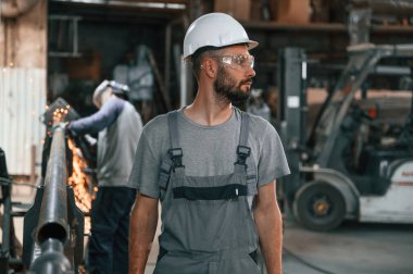 Arkada başka bir adam var. Gri üniformalı genç fabrika işçisi.