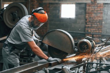 Yan görünüş, metali kesmek. Gri üniformalı genç fabrika işçisi.
