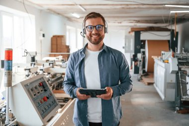 Kulaklıkla, tabletle. Yakışıklı adam ekolojik kutular üreten fabrikada çalışıyor..