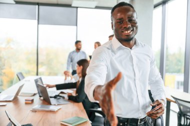 Dost canlısı siyah adam elini sıkmak için uzatıyor, selamlar. Bir grup ofis çalışanı içeride birlikte..