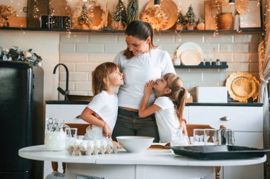 Mutfakta, çelenklerle birlikte. Anne ve iki küçük kızı yemek hazırlıyorlar..