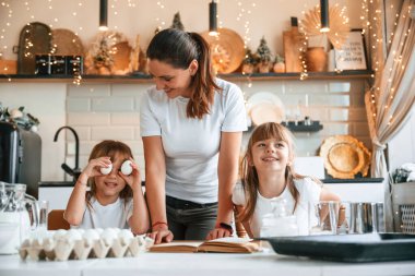 Mutfakta, çelenklerle birlikte. Anne ve iki küçük kızı yemek hazırlıyorlar..