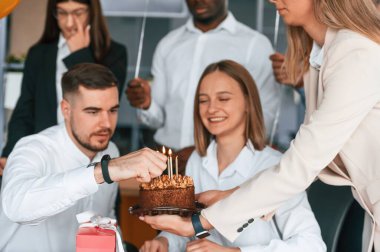 Pastanın üzerindeki mumları yakmak. Ofiste doğum günü olan bir çalışan, bir grup işçi..