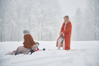 Kızak sürüşü. Anne ve kızı kış çayırlarında ve ormandalar..