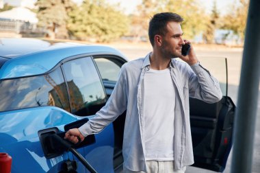 Telefonla konuşuyorum. Şarj istasyonunda mavi elektrikli arabası olan adam..