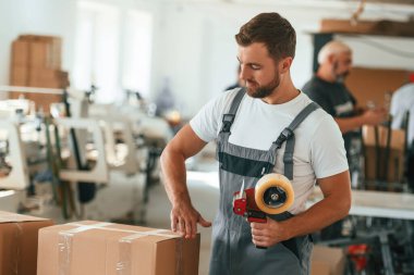 Gri üniformalı. Yakışıklı adam ekolojik kutular üreten fabrikada çalışıyor..