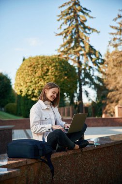 Öğrenme kavramı, dizüstü bilgisayarla oturmak. Gündelik giysiler içinde genç bir kız öğrenci dışarıda..