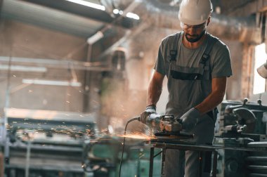 Açı öğütücü ellerinde. Gri üniformalı genç fabrika işçisi.