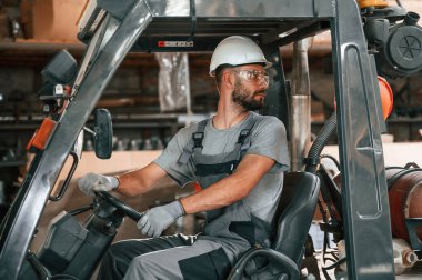 Forklift sürüyorum. Gri üniformalı genç fabrika işçisi.