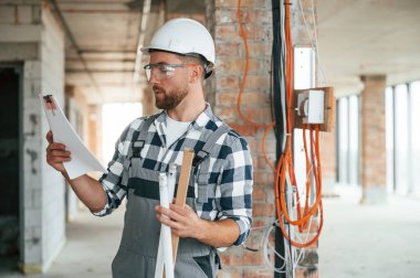 Projeyi planlıyorum, kağıtlarla. Bitmemiş odada üniformalı inşaat işçisi..