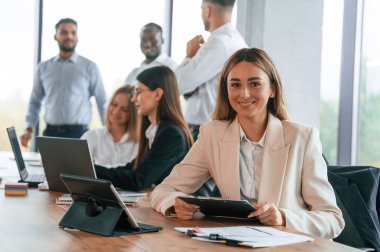 Masada not defteri ve tableti olan bir kadın var. Bir grup ofis çalışanı içeride birlikte..