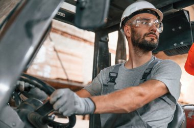 Profesyonel forklift sürücüsü. Gri üniformalı genç fabrika işçisi.